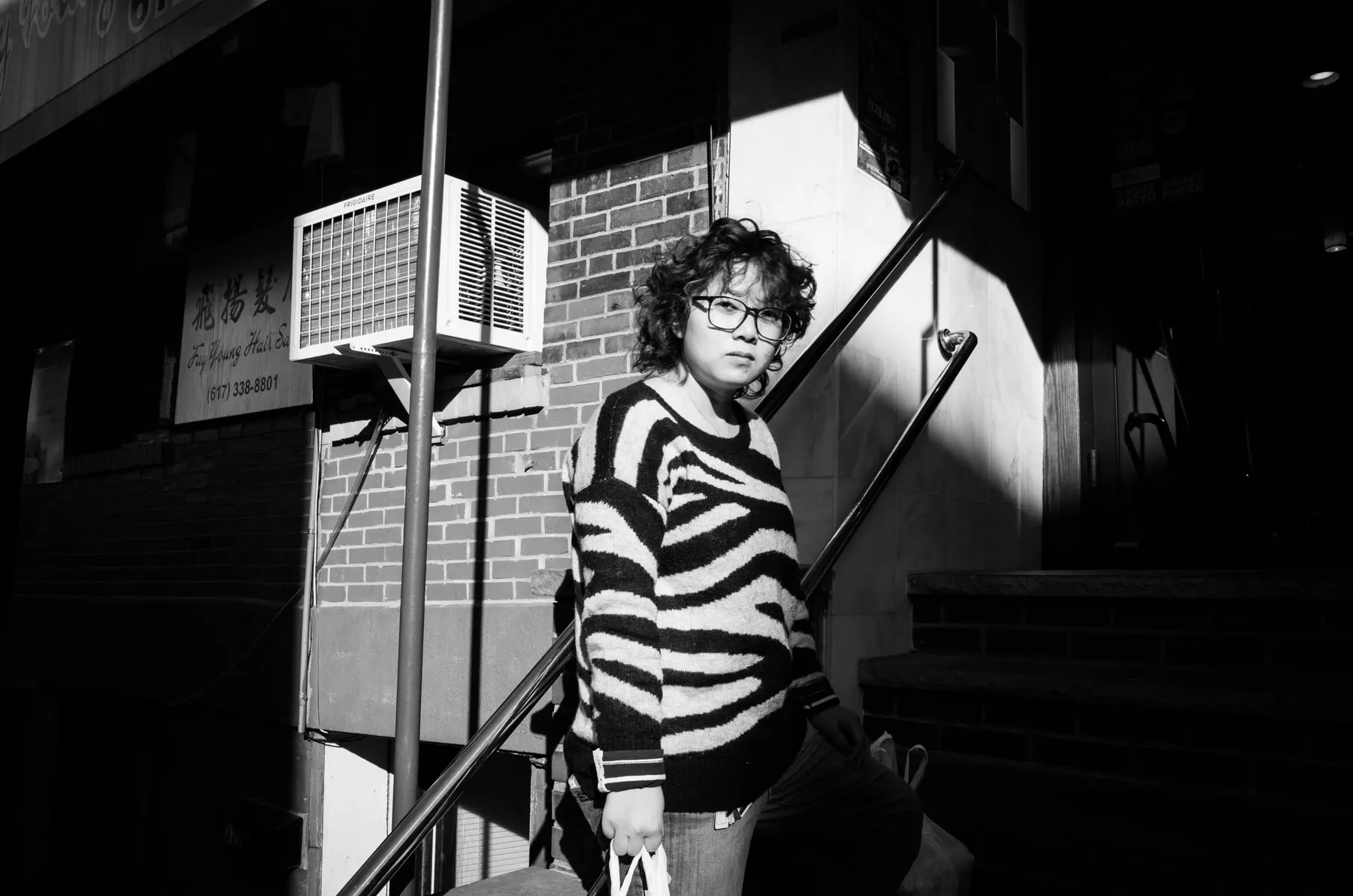 Woman in a zebra-striped sweater on basement steps below a Chinatown hair salon