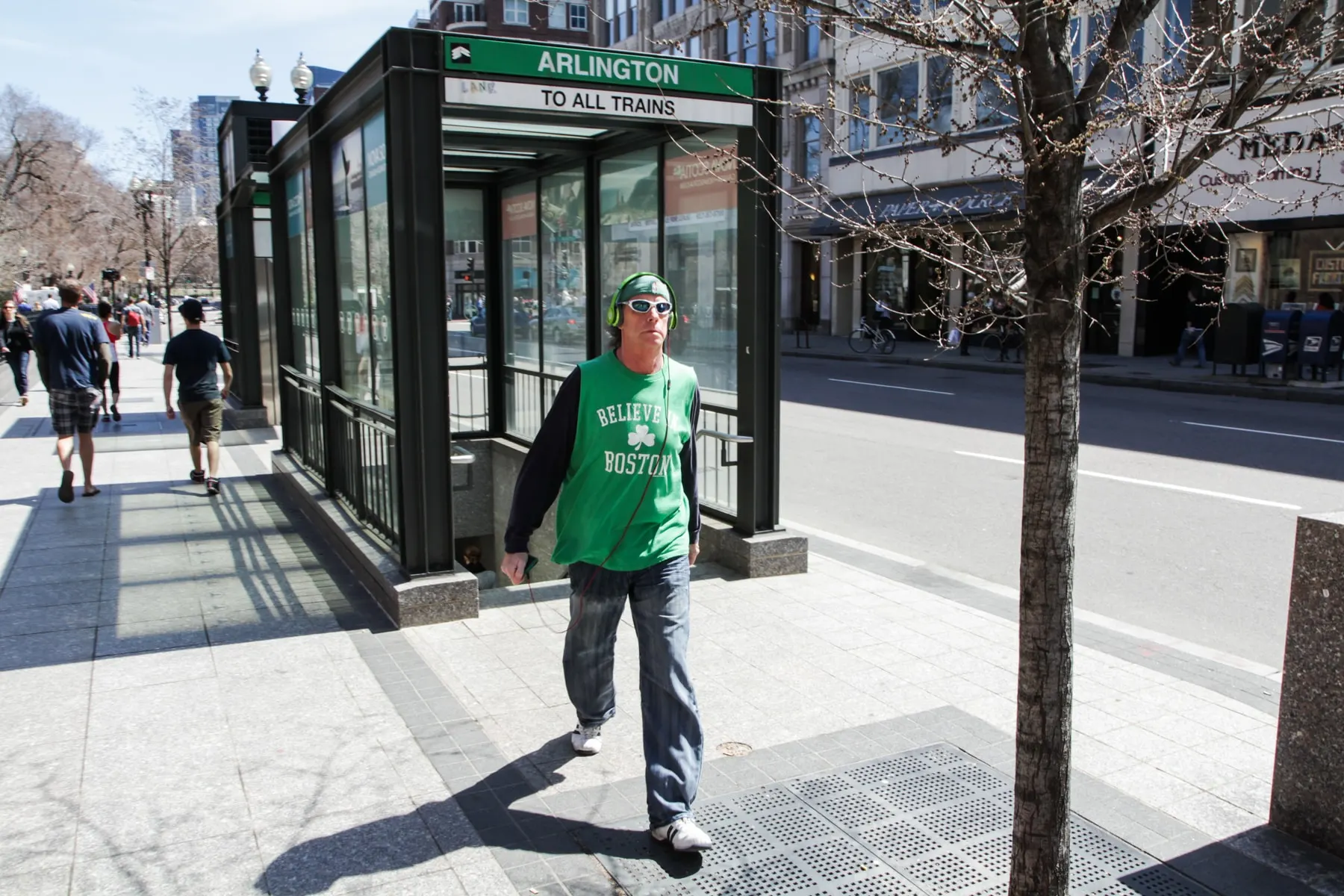 Man in a green shirt crosses a plaza beside a subway entrance