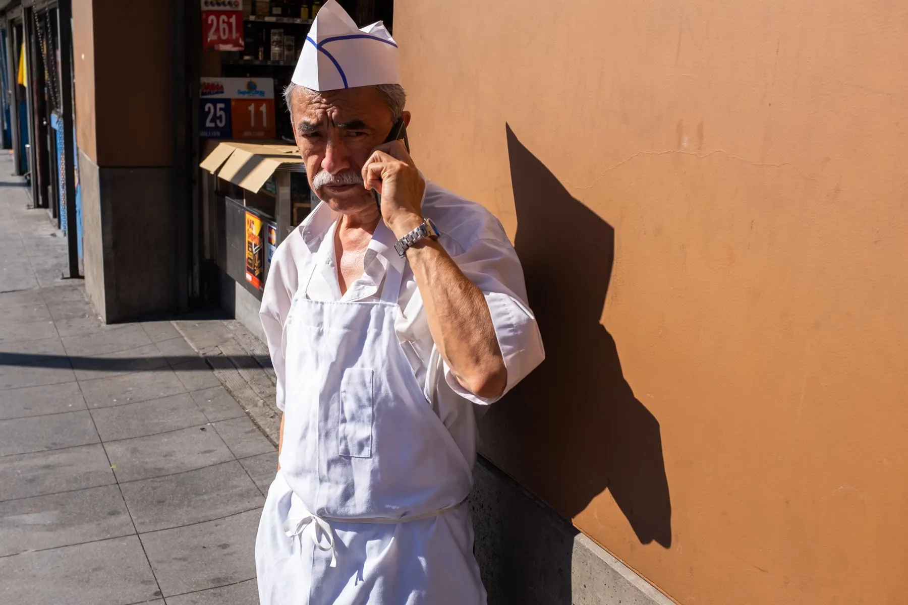 Butcher in a white apron and paper hat takes a phone call against an orange wall