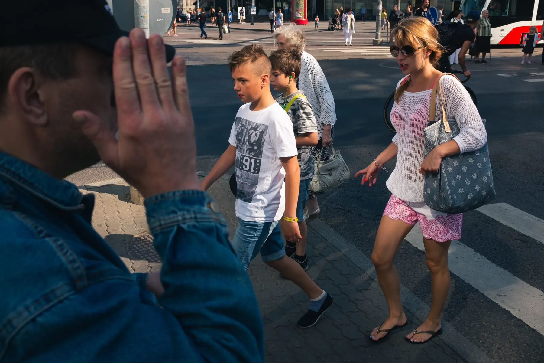 Man raises a hand towards the camera as a family crosses behind him