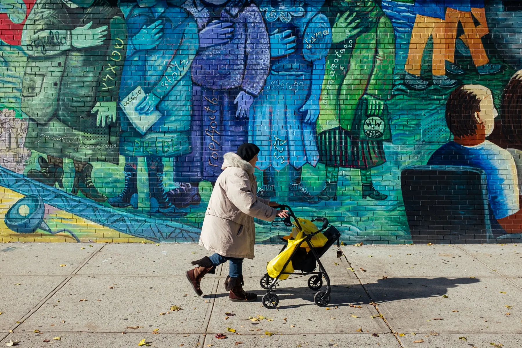 Woman pushes a yellow stroller past a blue and green painted mural