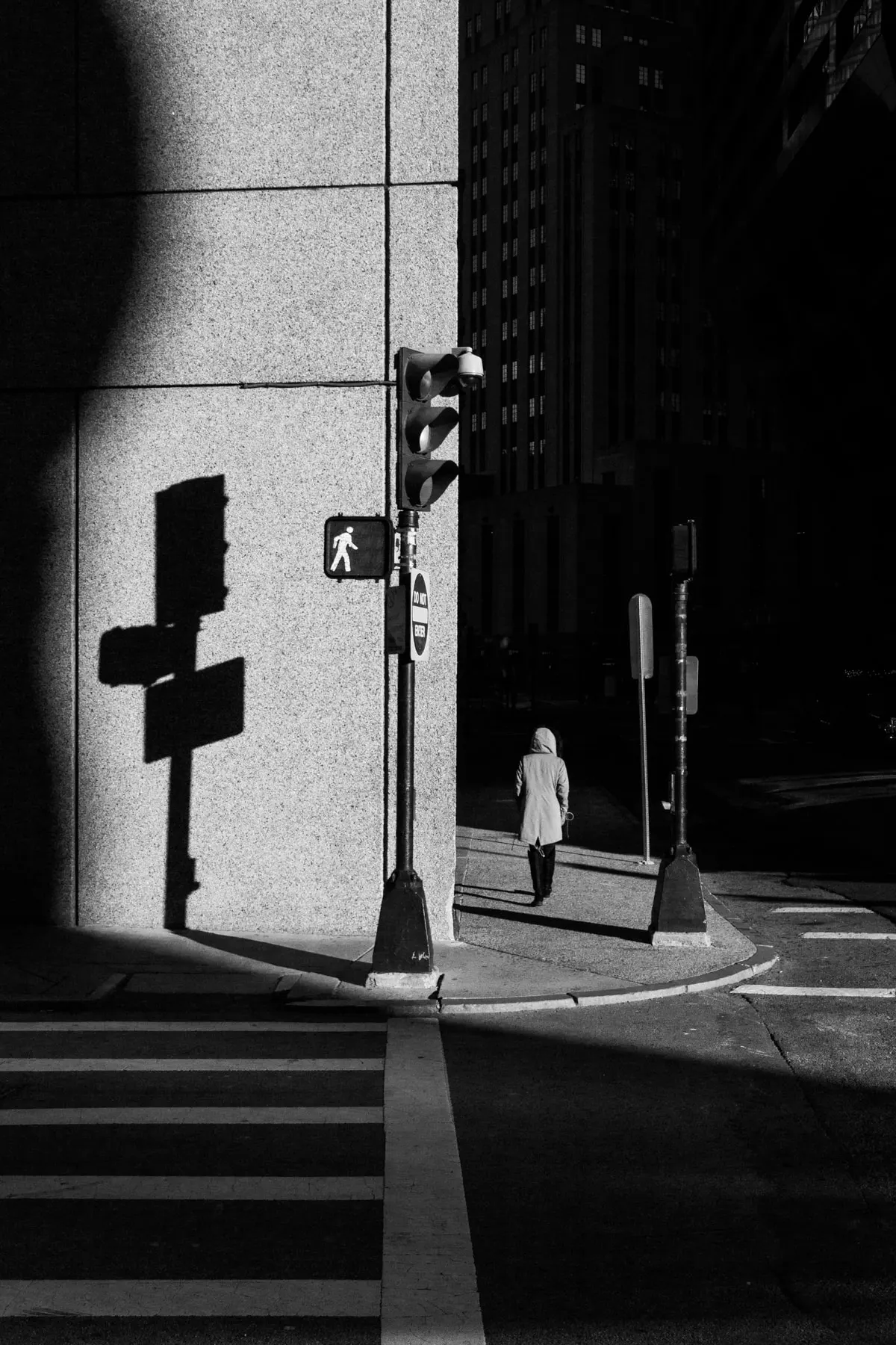 Woman waits to cross while a traffic signal throws a long shadow up a wall
