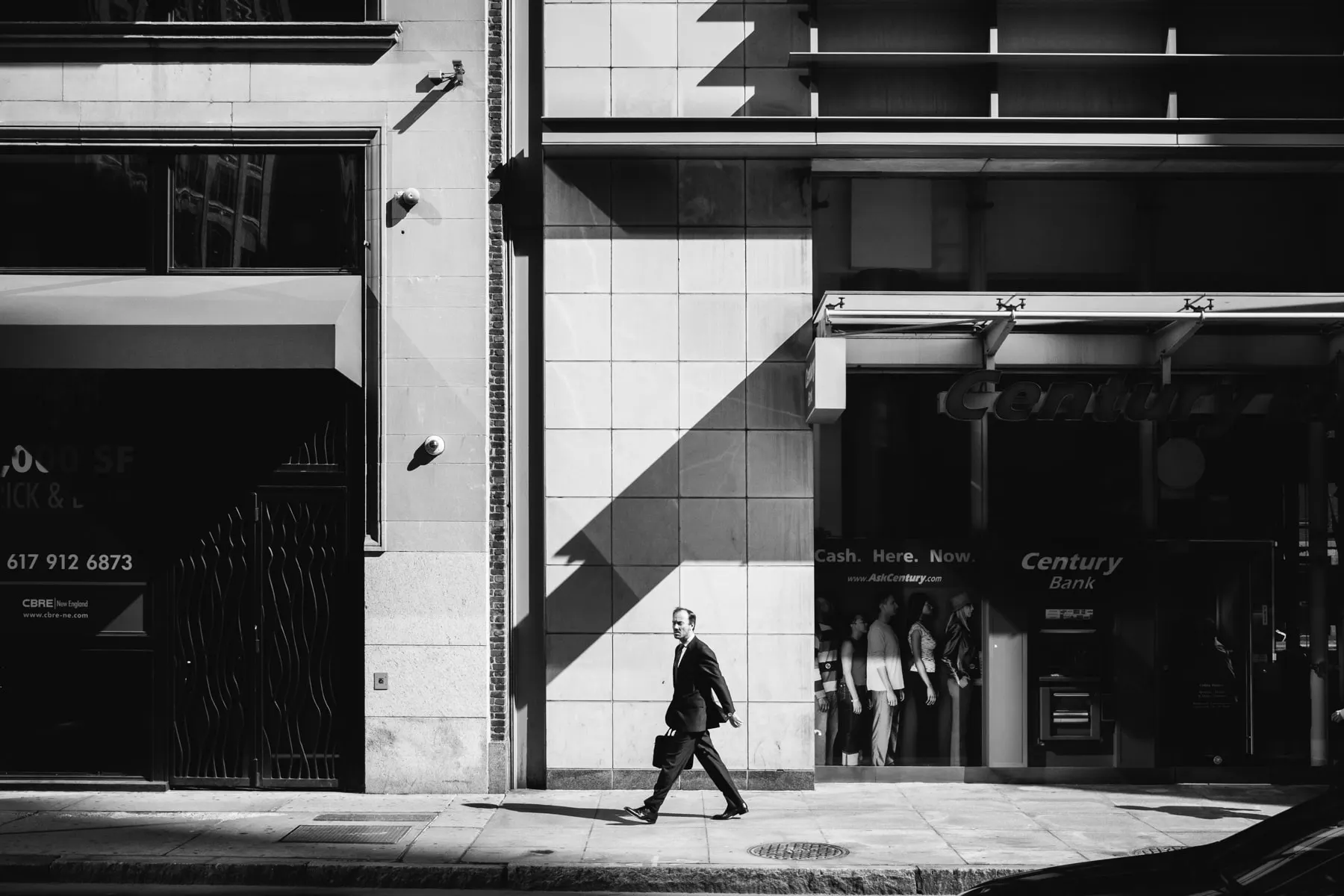 Man in a suit walks past a bank entrance framed by hard geometric shadows