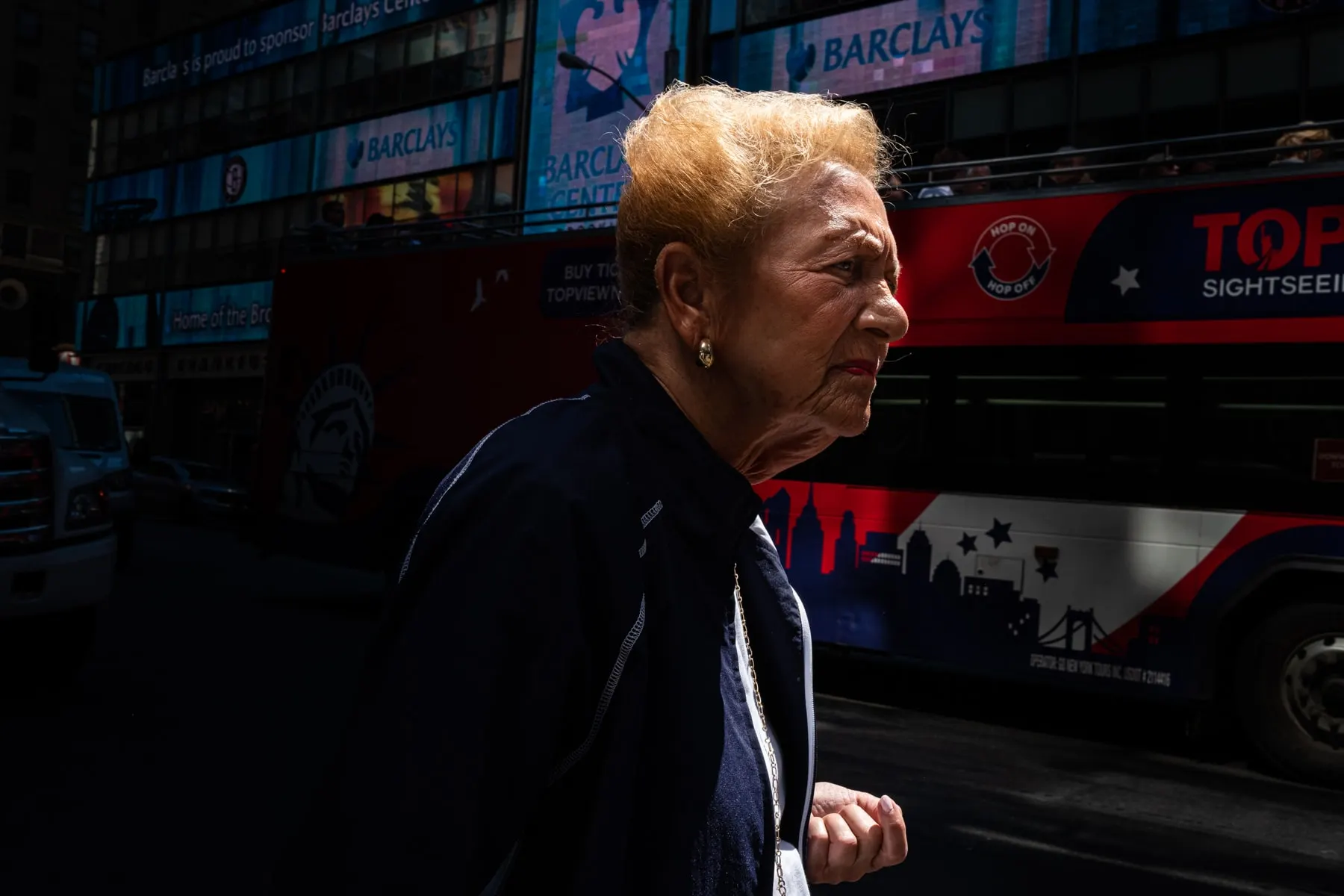 Woman with cropped blonde hair walks past a red sightseeing bus