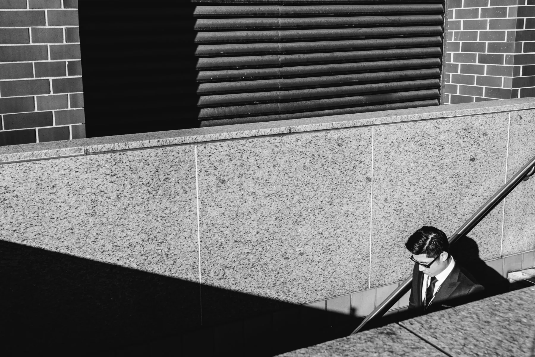 Man in a suit sits at the foot of a steep granite wall cut by a diagonal shadow
