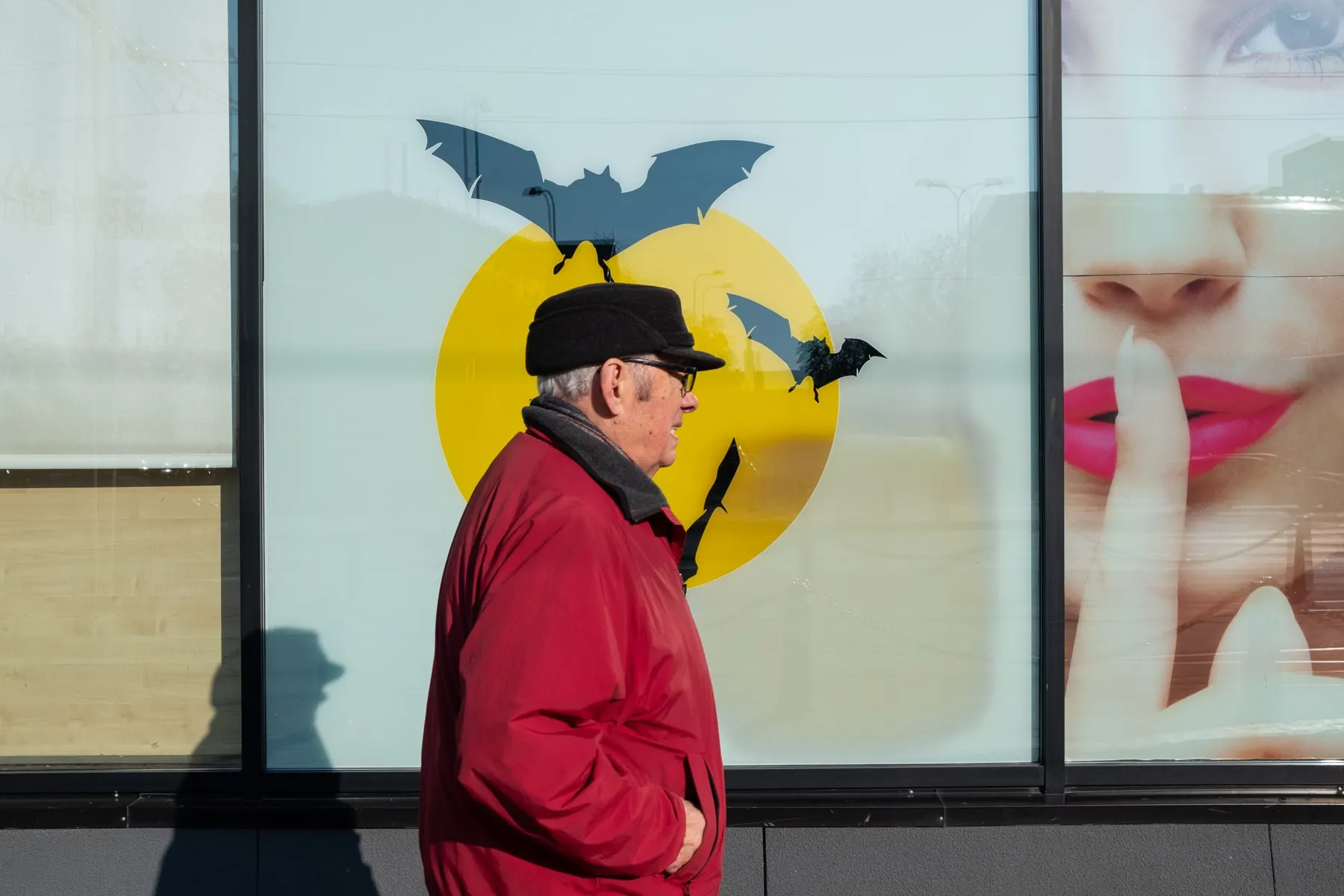 Man in a red jacket walks past a shop window printed with bats and a yellow moon
