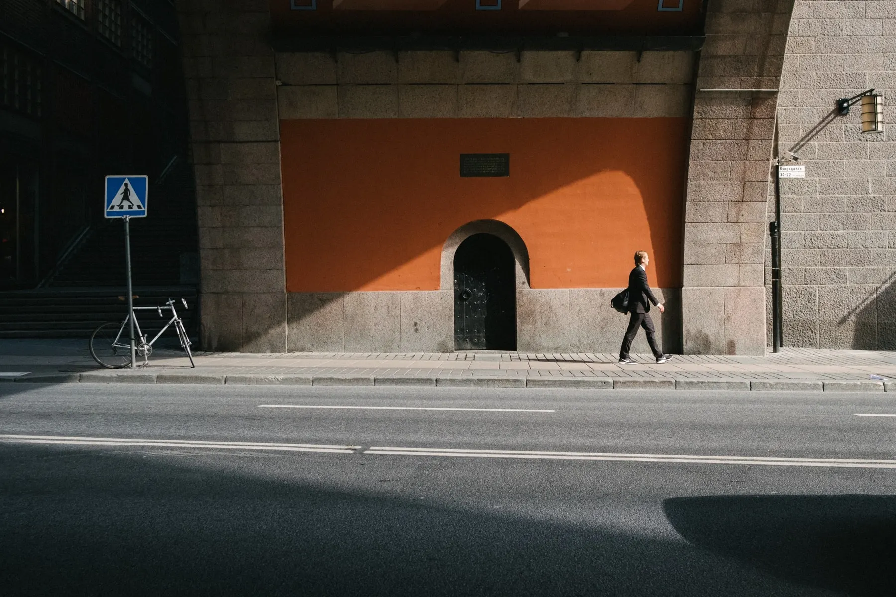 Man crosses a bare pavement below a wide orange archway