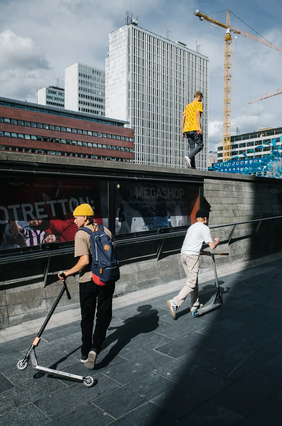 Boys on scooters at the foot of a concrete ramp, another walking the top edge