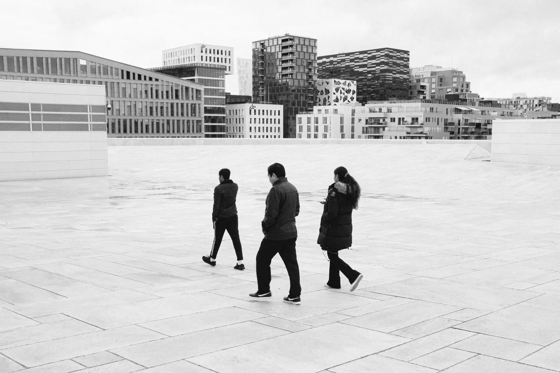 Three people walk apart across an empty stone plaza below new buildings