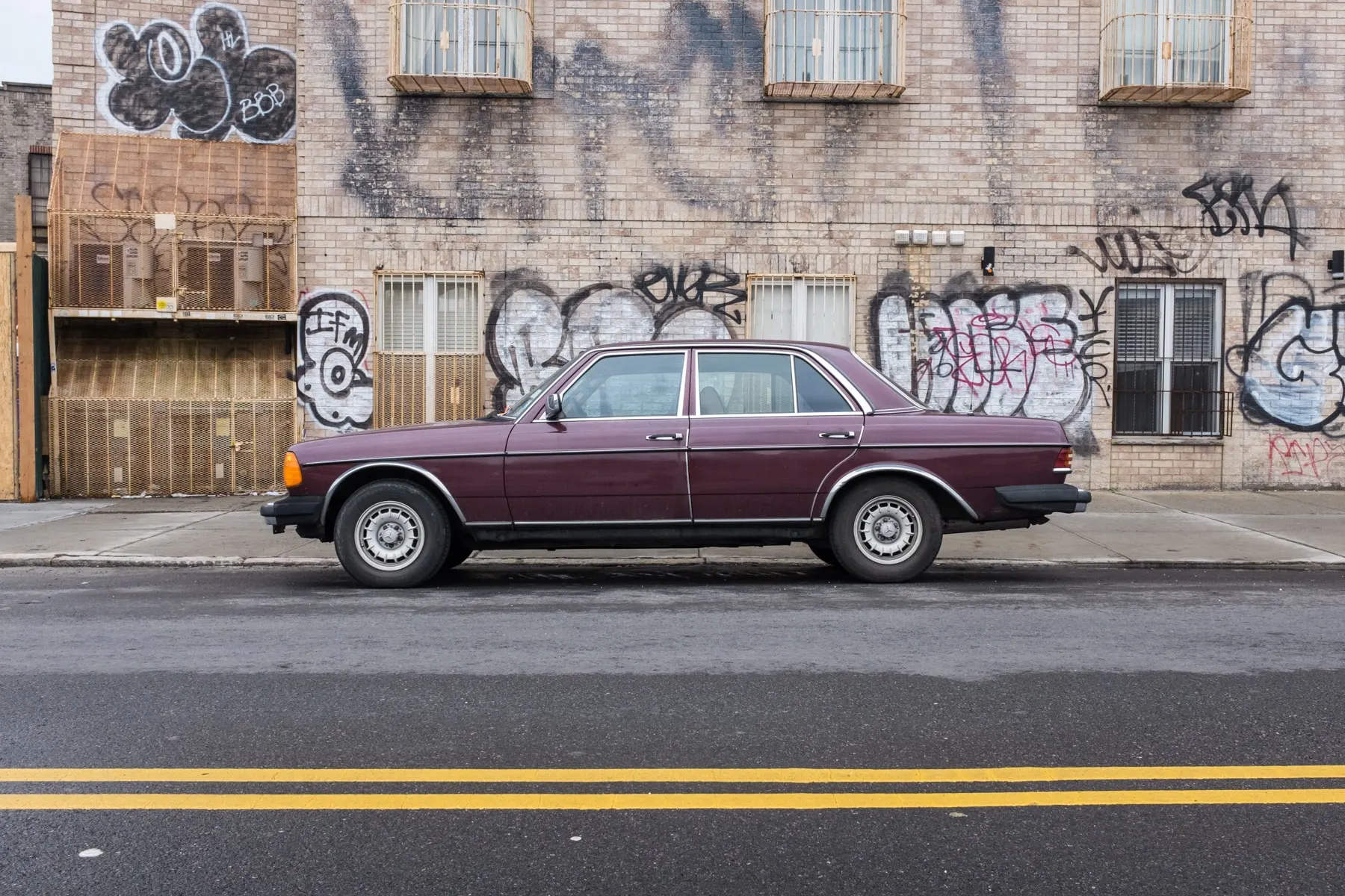 Maroon Mercedes sedan parked along a graffitied brick wall
