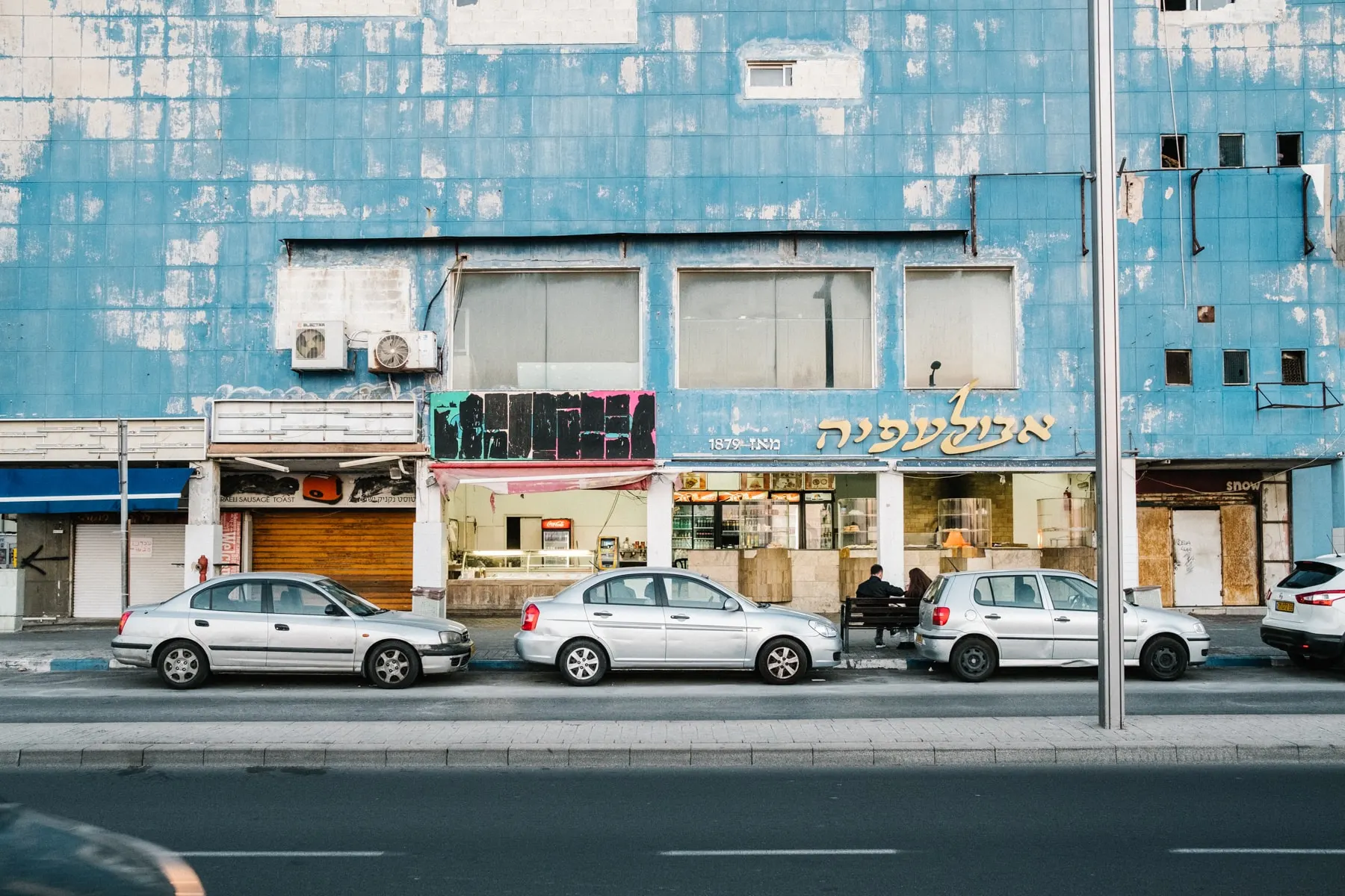 Cars parked along a blue-tiled shopfront