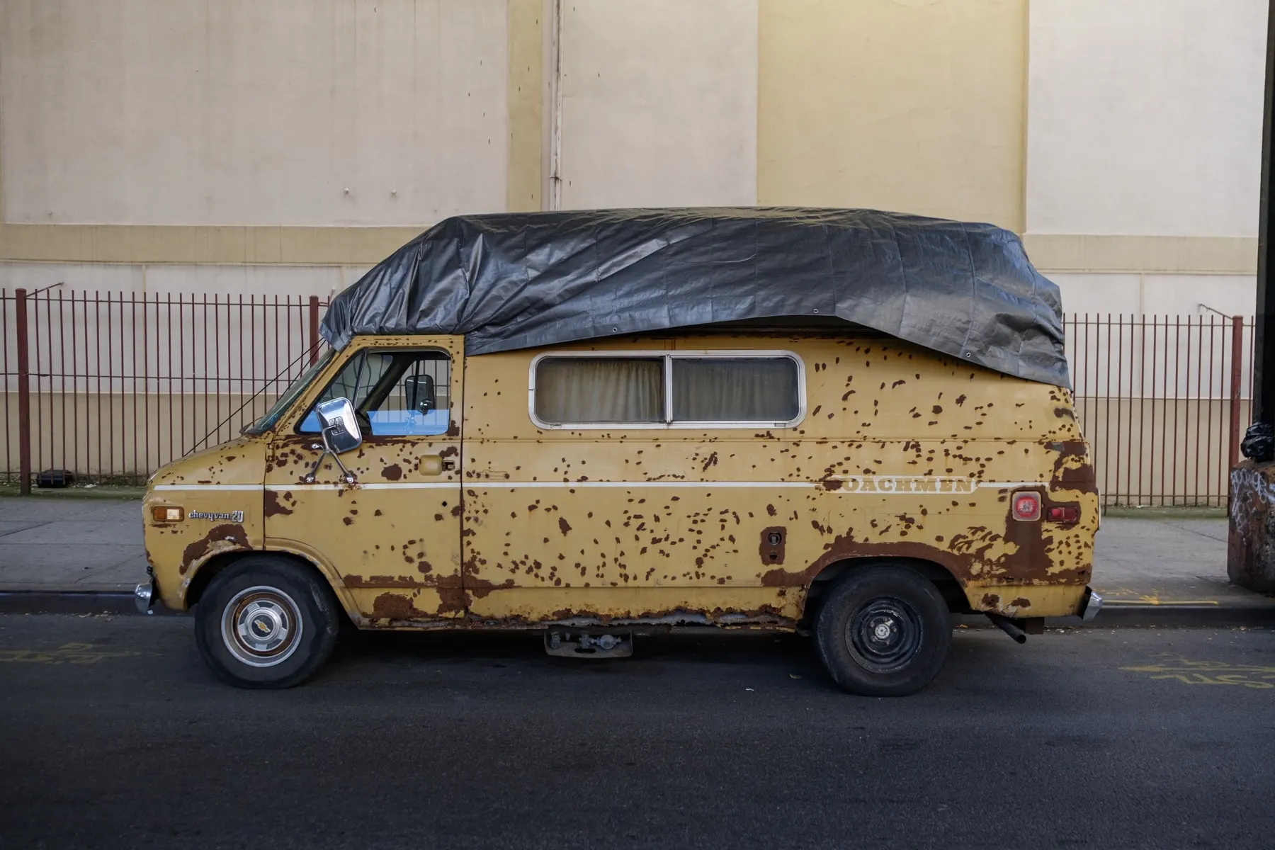 Rusted yellow camper van with a tarpaulin over the roof