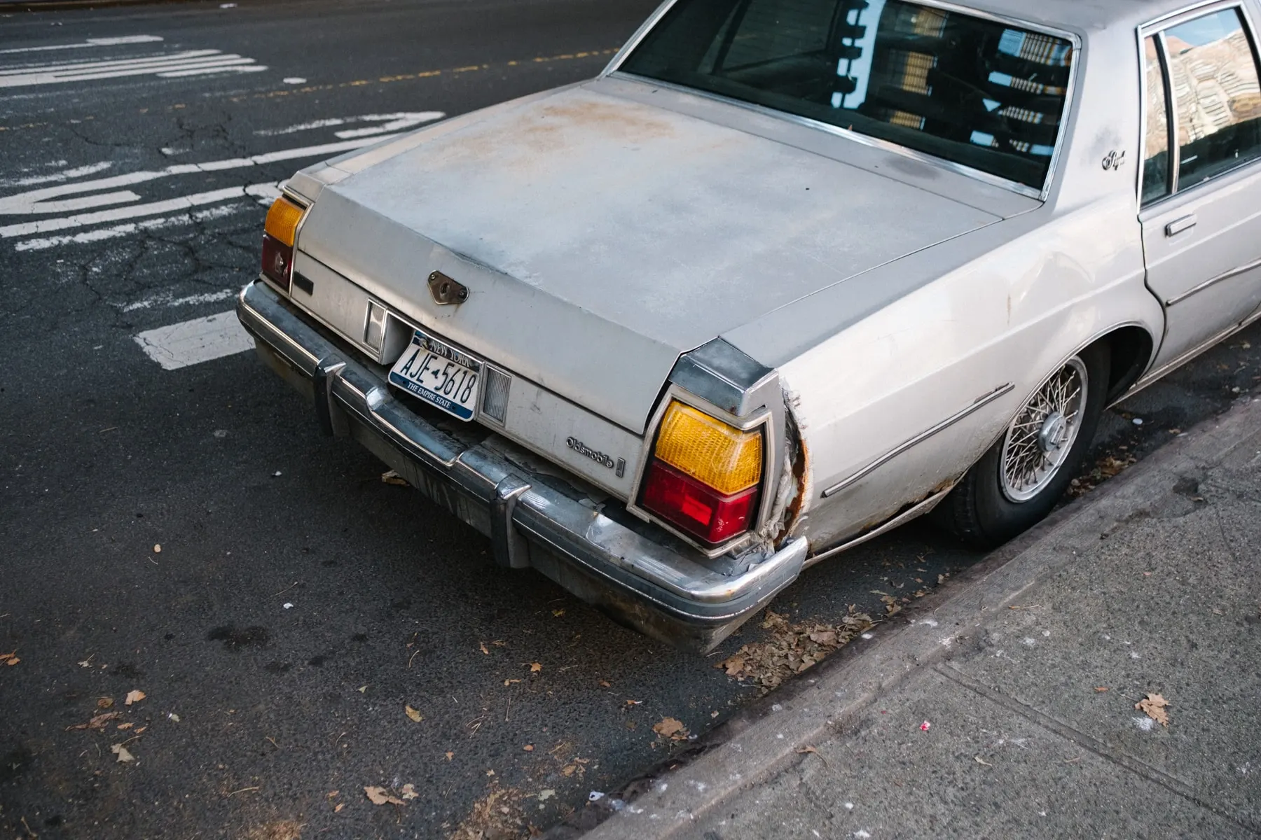 Rear of a white sedan parked at the kerb, leaves on the ground