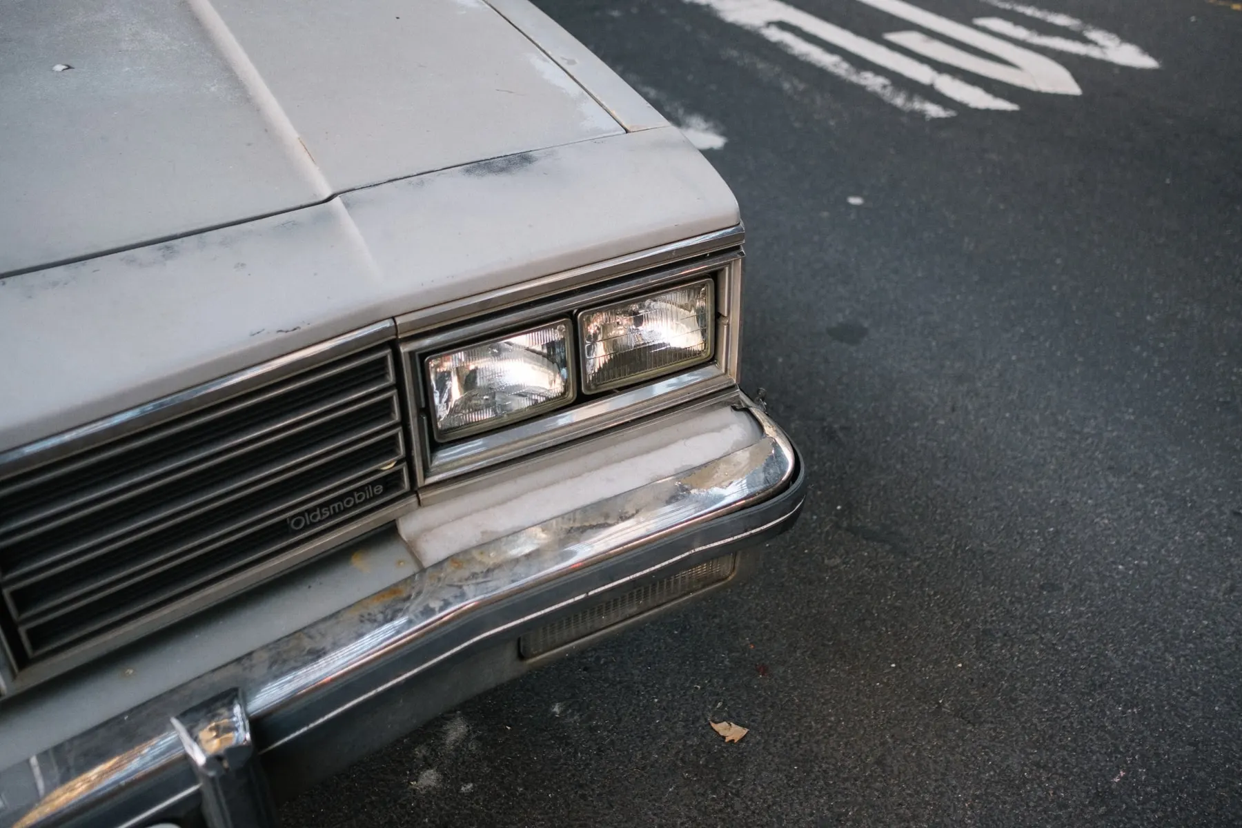 Front corner of a grey Oldsmobile on wet tarmac