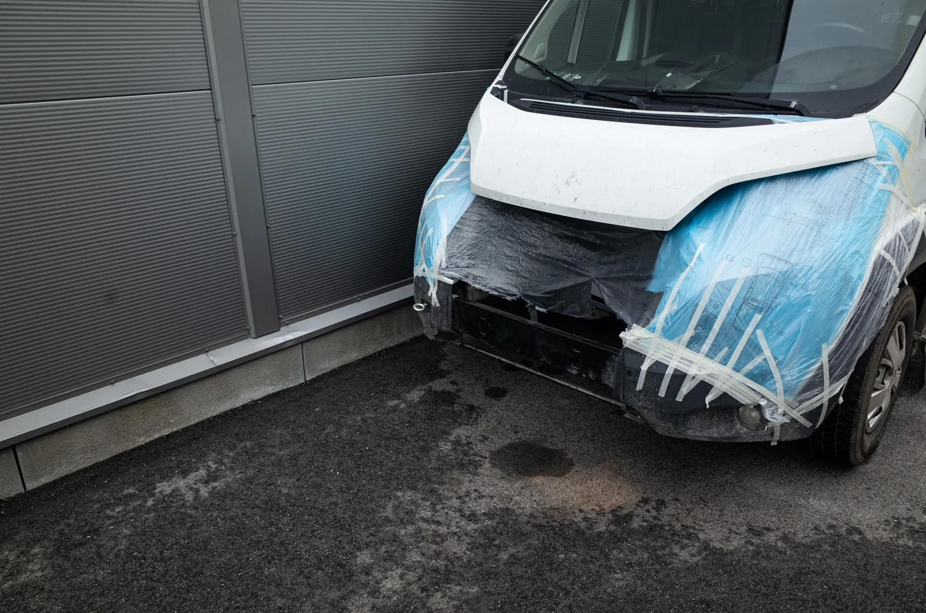 Van with its front wrapped in plastic beside a metal wall