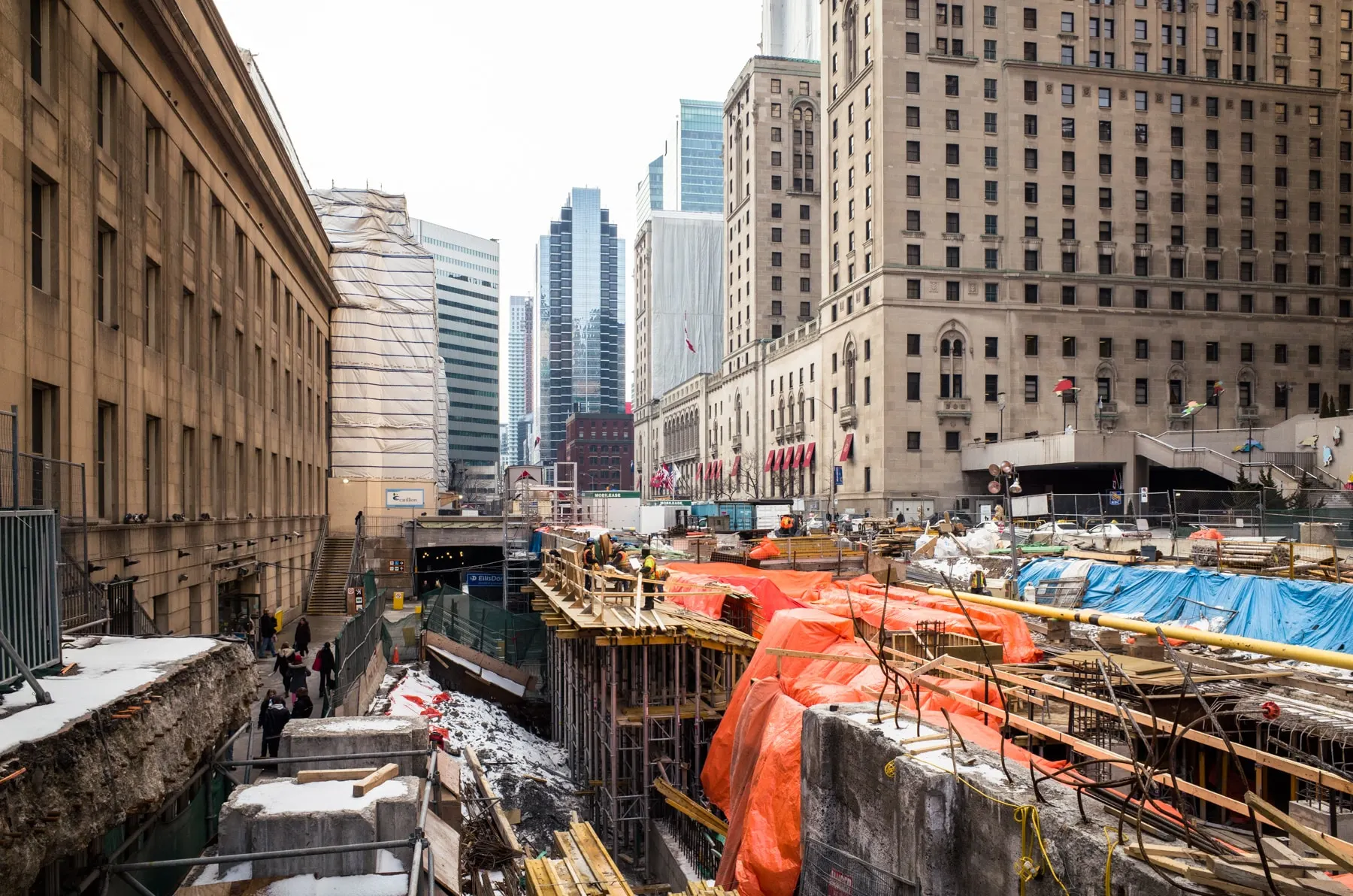 Construction pit covered in orange tarpaulin below city towers