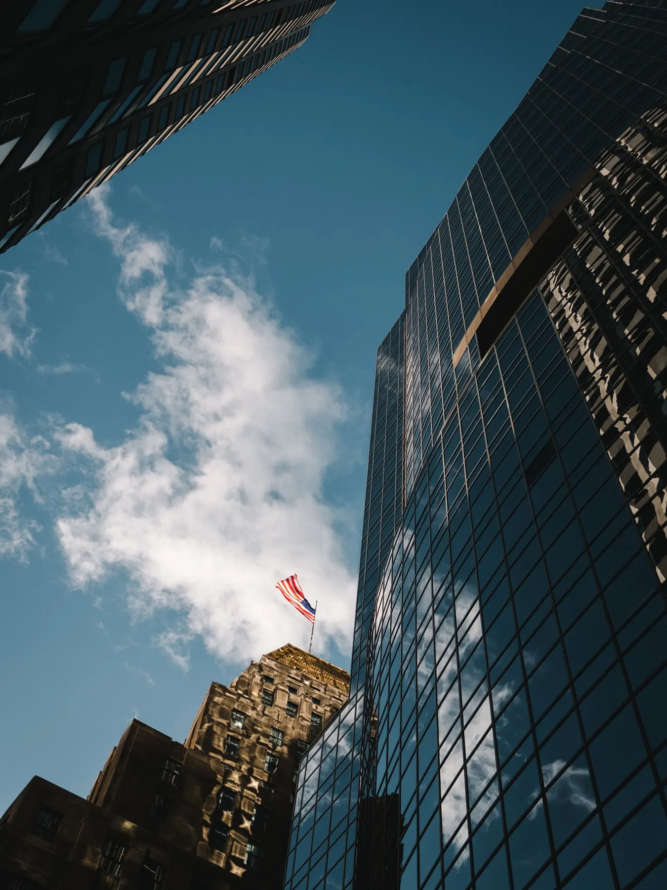 Glass tower and a flag seen from below against blue sky and cloud