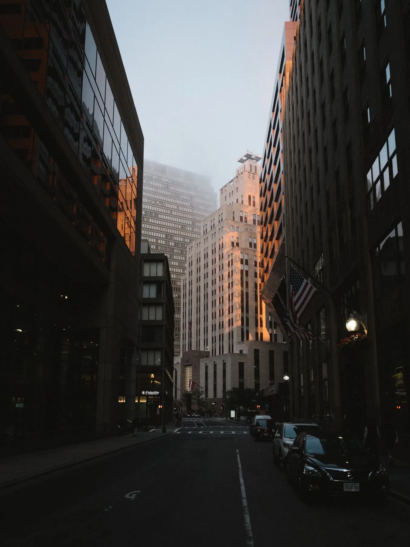 Narrow street at dusk with lit facades and parked cars
