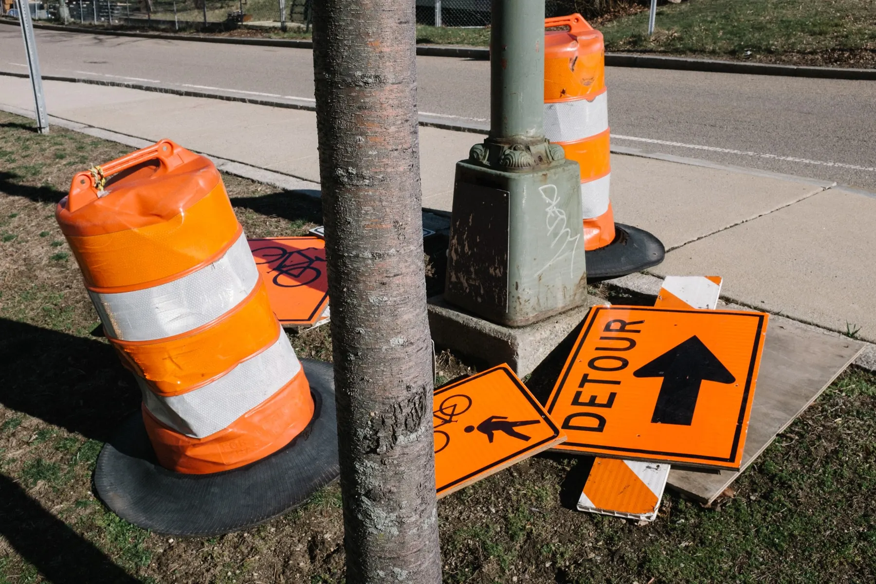 Barrel, cone and a detour sign propped by a tree