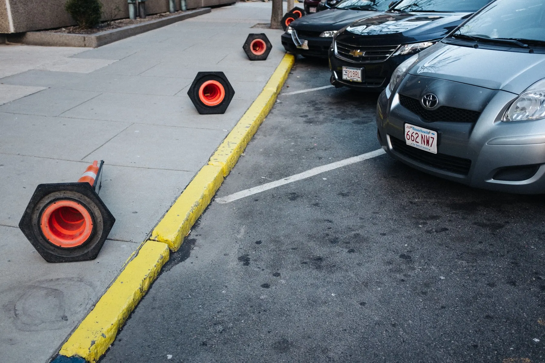 Cone and rubber bases on a kerb beside parked cars