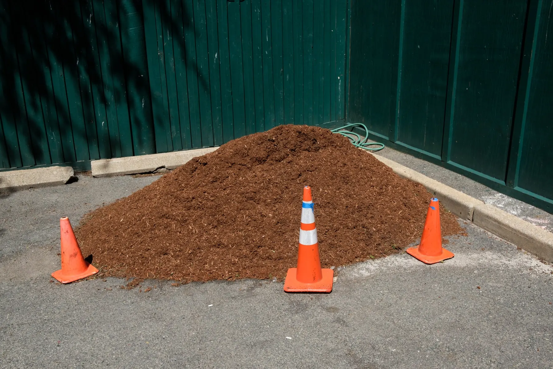 Cones around a mound of wood chips against a green hoarding