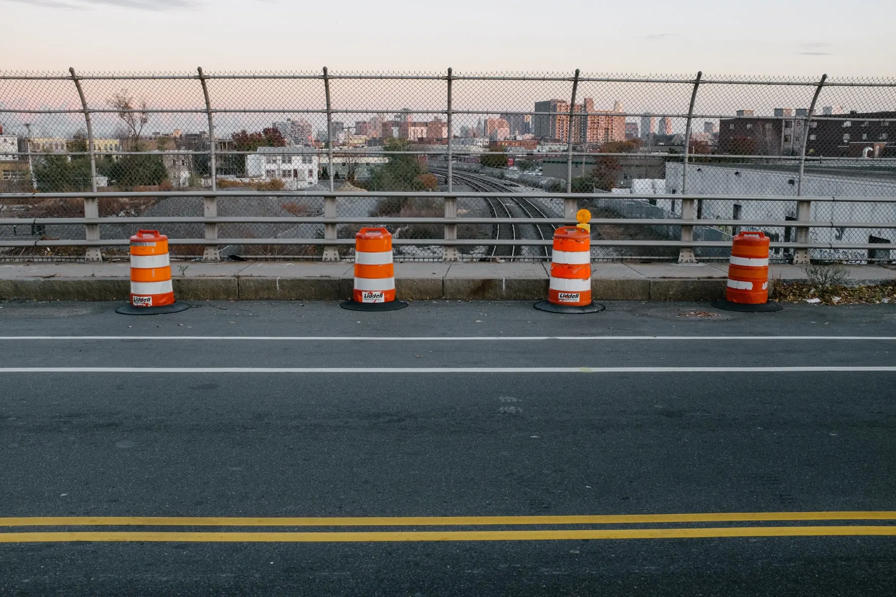 Barrels along a bridge railing above railway tracks and a distant skyline